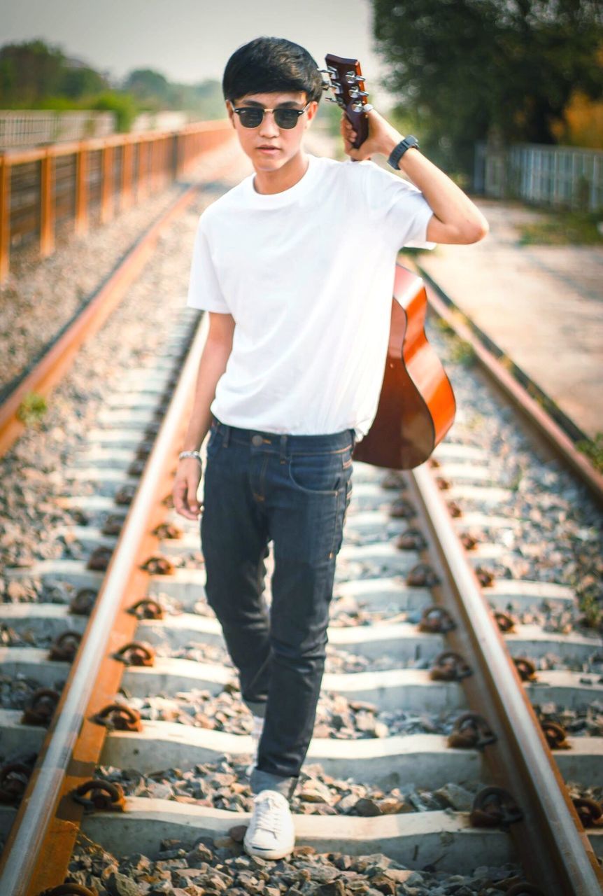 railroad track, casual clothing, lifestyles, rail transportation, focus on foreground, standing, full length, person, leisure activity, front view, looking at camera, transportation, young adult, portrait, railing, public transportation, day, warm clothing