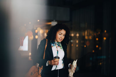 Mid adult businesswoman holding food and drink while walking in cafe