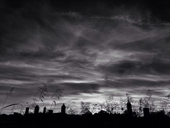 Silhouette of trees on landscape against cloudy sky