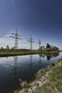 Electricity pylon by lake against sky