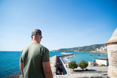 Rear view of man looking at sea against clear blue sky