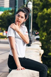 Portrait of young woman touching lips while sitting on retaining wall