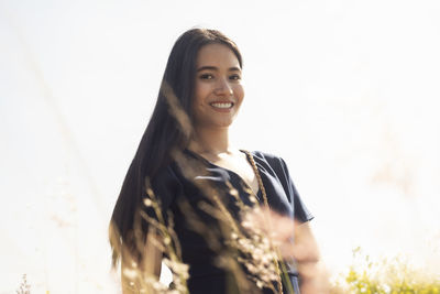 Portrait of young woman with long hair standing against clear sky