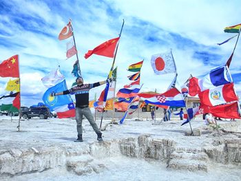 Mid adult man with arms outstretched standing against various flags