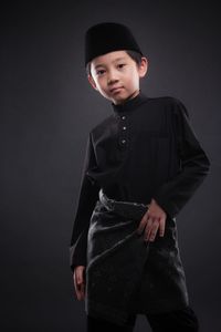 Portrait of boy standing against black background