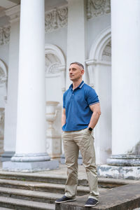 A man in casual clothes stands near the columns of a white building