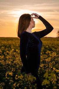 Woman standing on field against sky during sunset