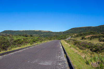 Country road leading towards mountains against blue sky