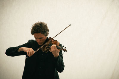 Man playing violin while standing against wall