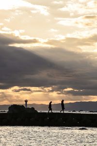 Silhouette people walking on pier by sea against sky during sunset