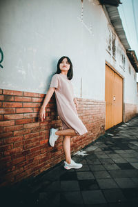 Full length portrait of woman standing against wall