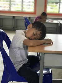 Side view of boy sitting on table while sleeping 