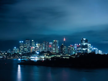 Illuminated city by sea against sky at night