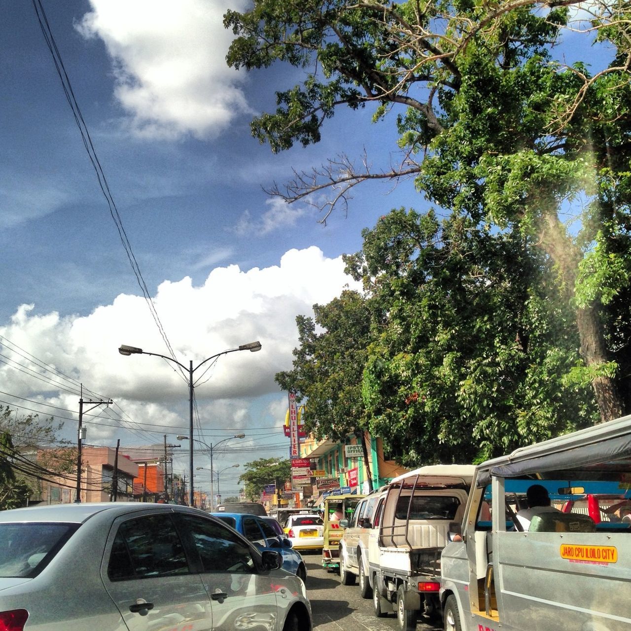 transportation, car, land vehicle, mode of transport, tree, road, street, on the move, sky, road marking, traffic, the way forward, travel, cloud - sky, city, city street, built structure, street light, architecture, building exterior