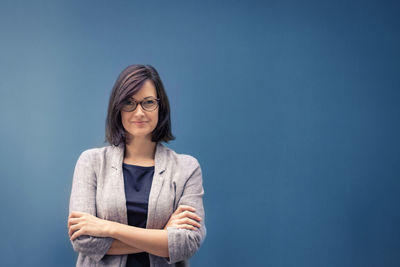 Portrait of confident smiling businesswoman with arms crossed standing against blue wall