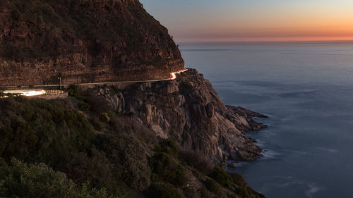 Light trails on mountain road by sea during sunset