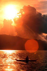 Silhouette boating in calm lake at sunset