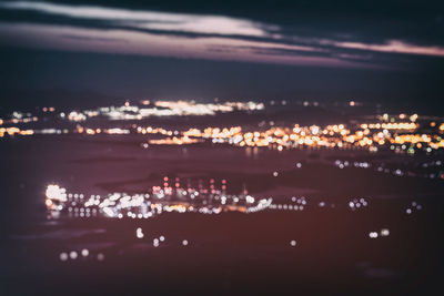 Aerial view of illuminated city by sea against sky at night