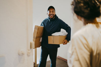 Happy male delivery person arriving with parcels at doorstep