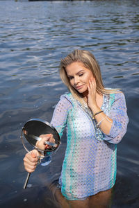 Woman holding hand mirror kneeling in lake