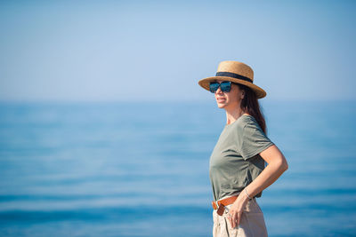 Side view of woman wearing hat standing against sea