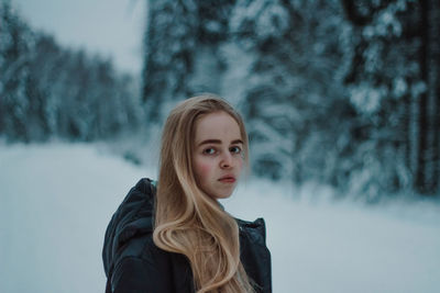 Portrait of young woman standing against trees during winter
