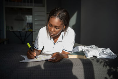 Ethnic student doing homework on bed