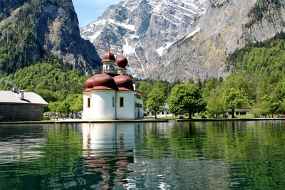 Reflection of st bartholomew church in lake against mountains on sunny day