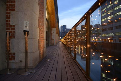 Illuminated footbridge by building at dusk