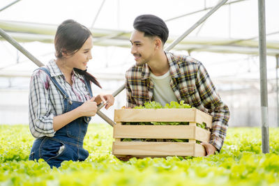 Smiling man holding container with vegetable while talking with woman at farm