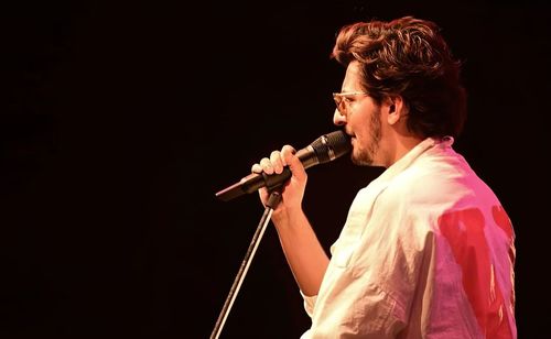 Side view of man singing against black background