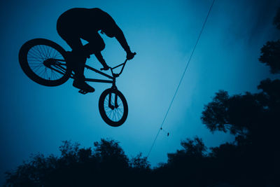 Low angle view of silhouette person flying bicycle against sky