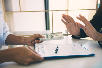 Cropped hands of businessman bribing male coworker at desk in office