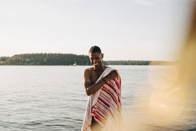 Portrait of young man standing in lake against sky