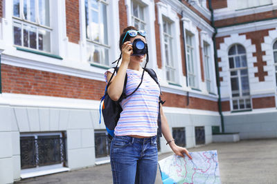 Woman photographing while standing against building