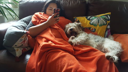 Woman using mobile phone while relaxing by dog on sofa at home