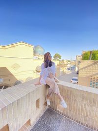  woman sitting on railing against clear sky