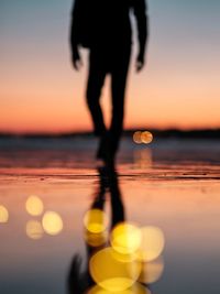 Low section of silhouette man standing by sea at sunset