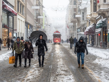 People walking on wet street in city during winter