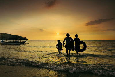 Silhouette people on beach against sky during sunset