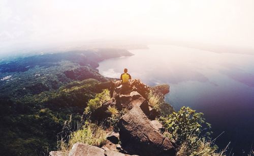 High angle view of man sitting on mountain against sea during sunny day