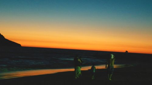 Silhouette people by sea against sky during sunset