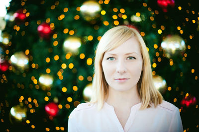 Close-up portrait of young woman smiling while standing by christmas tree