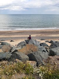 Rear view of boy sitting on rock at beach