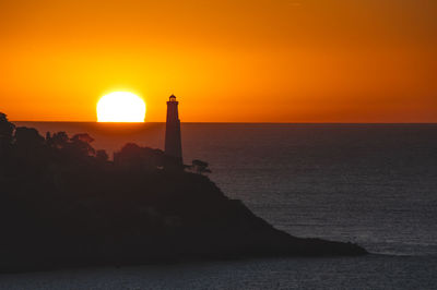 Lighthouse by sea against sky during sunset