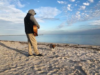 Man playing guitar while standing with dog on shore at beach