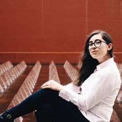 Portrait of young woman sitting against wall