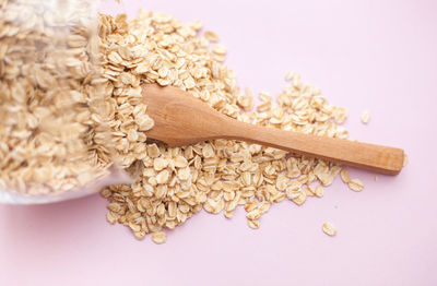 High angle view of oats in wooden spoon on pink background