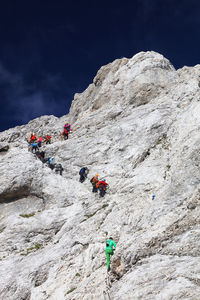 Low angle view of people climbing on mountain against sky