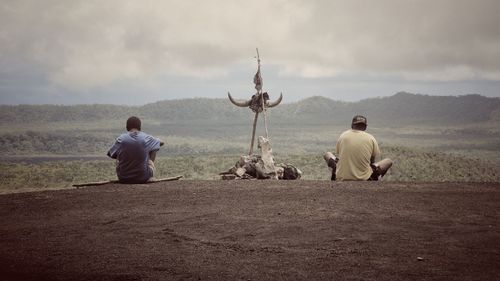 Man sitting on mountain against cloudy sky